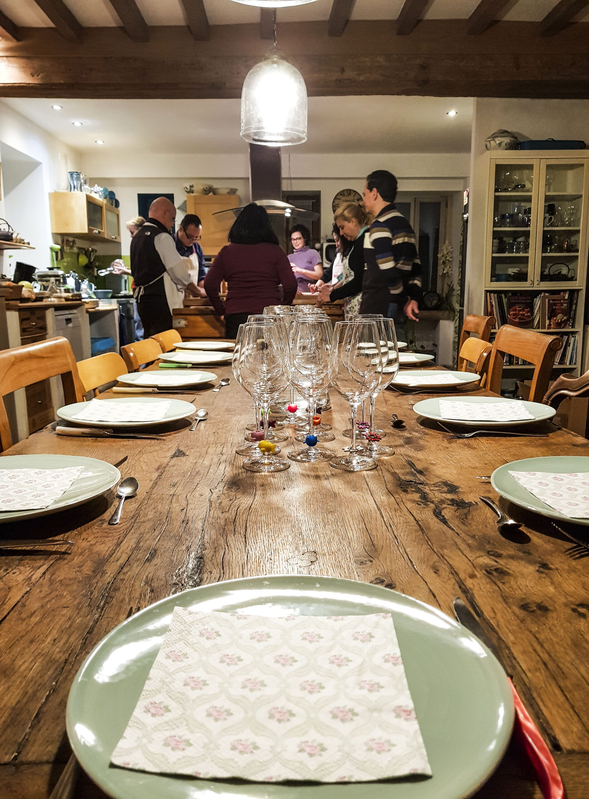 Burgundy cooking experience In the foreground, a table set with plates, cutlery, and glasses.
In the background, several people taking a cooking class in the kitchen.
Burgundy cooking experience